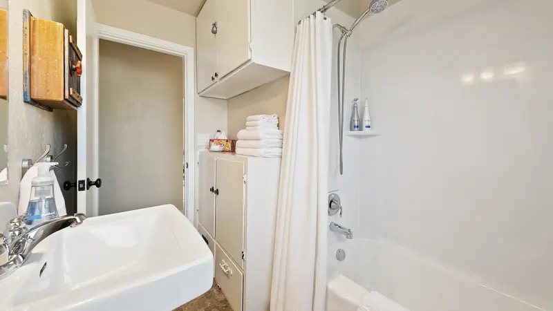 Bathroom with a pedestal sink, a tub with a shower curtain, and a towel cabinet.