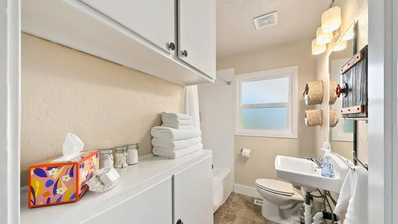 Bathroom shelves with towels and tissues, a pedestal sink, a toilet and a window.