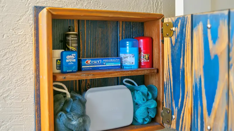 Open bathroom cabinet with toothpaste, deodorant and other toiletries.