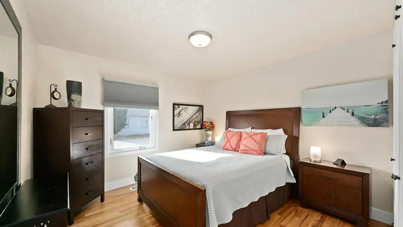 Bedroom with a queen bed, coral pillows, two nightstands with lamps and a tall dresser.