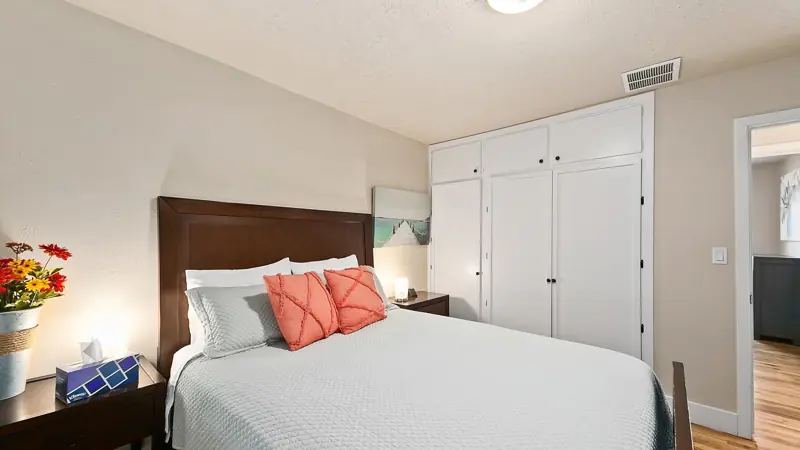 Queen bed with coral pillows and built-in white closets along the wall.
