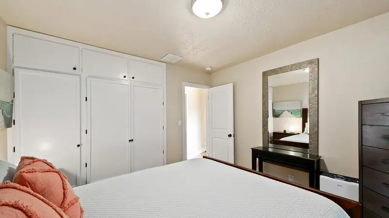 Bedroom with built-in white closets, a standing mirror and a dresser.