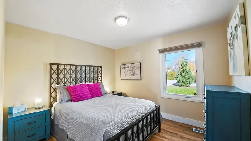 Second bedroom with a queen bed, pink pillows, a teal nightstand and a window.