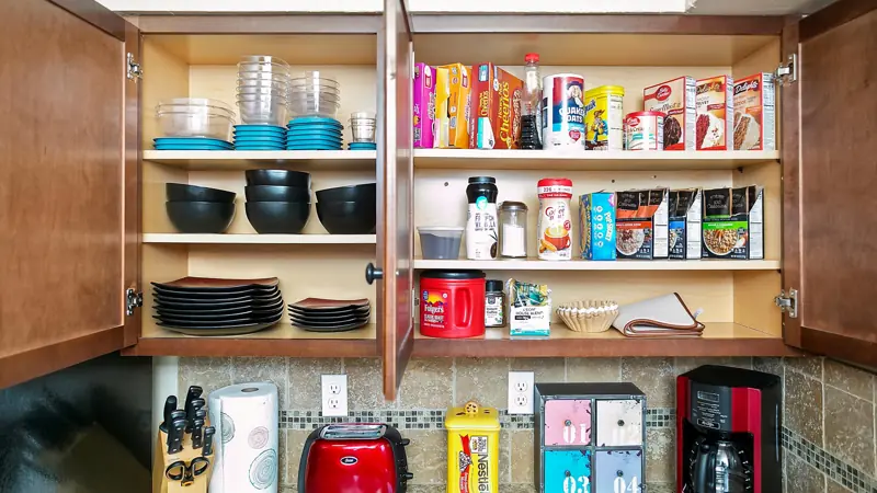 Open kitchen cupboards stocked with bowls, plates, containers and food staples.