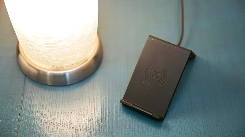 Bedside lamp next to a wireless phone charger on a nightstand.