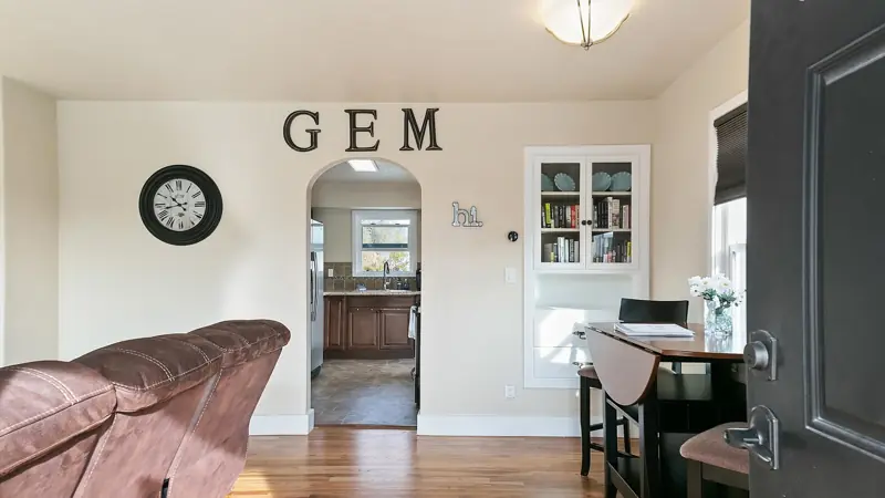 Dining area with a wall clock and large GEM letters, and an arched doorway to the kitchen.