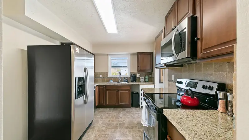 Kitchen with a stainless refrigerator, an electric range with a red kettle, and a microwave.