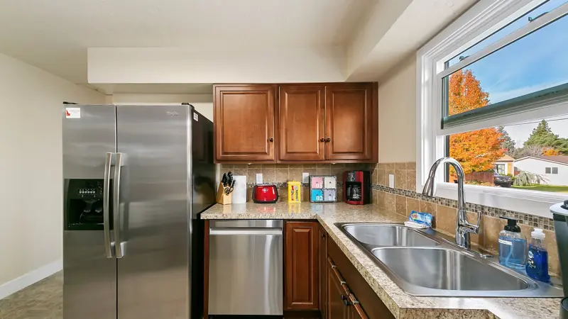 Kitchen corner with a stainless dishwasher, a double sink under a window, and a coffee maker.