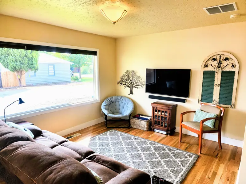 Living room with a large front window, a wall-mounted TV, a round chair and an armchair on a patterned rug.