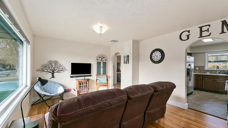 Living room with a brown reclining couch, a large window and an open doorway to the kitchen.