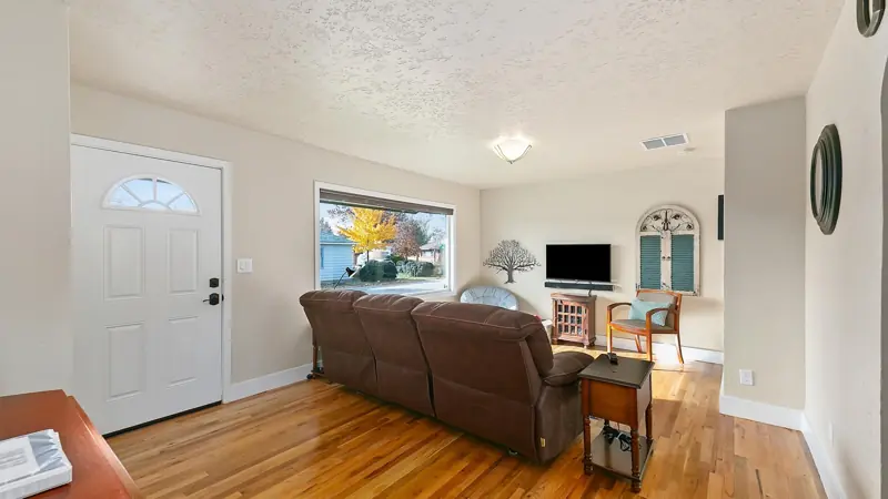 Front door opening into the living room, with a brown reclining couch and hardwood floors.