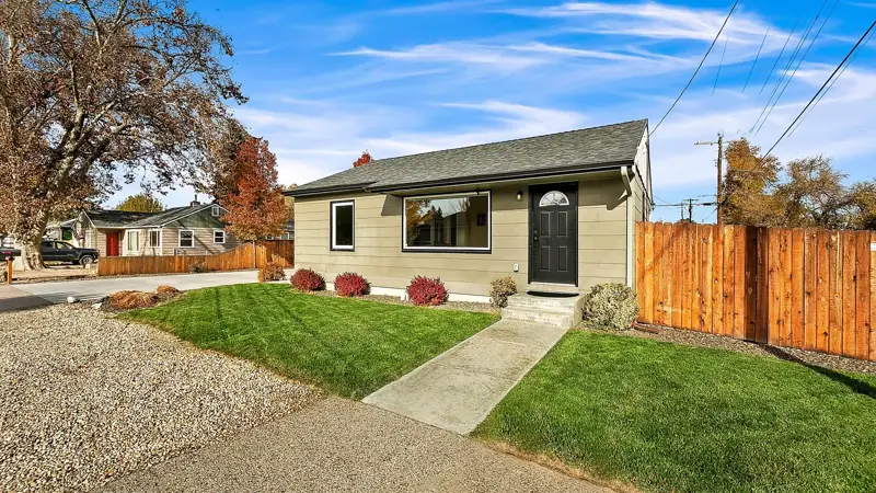 Front of the single-story home with a lawn, a walkway and a wood fence.