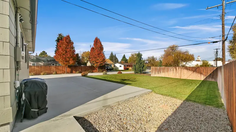 Side of the home with a covered grill, the driveway and a fence.