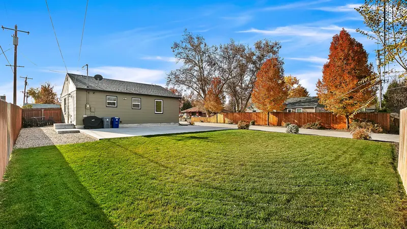Large green backyard lawn with the home and autumn trees behind it.