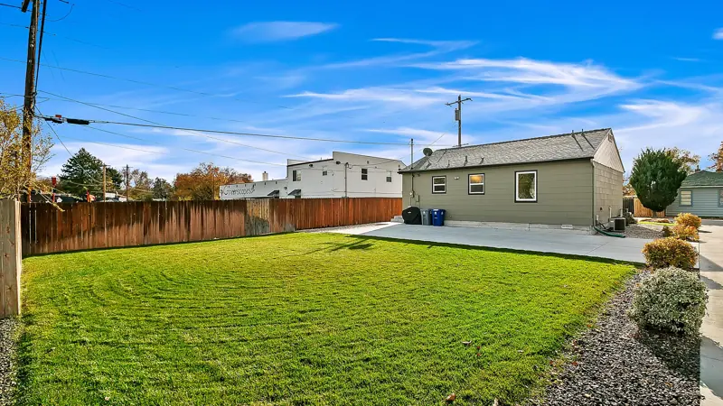 Backyard lawn bordered by a wood fence, with the home in the distance.