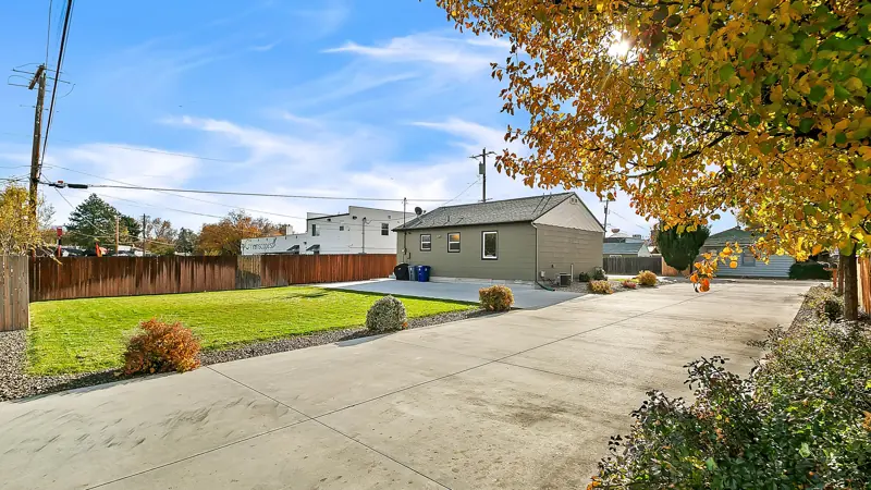 Long concrete driveway and parking pad beside the lawn under an autumn tree.